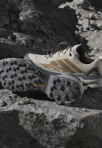 Scarpe da trekking beige e tan con suole nere Continental robuste, poggiate su un terreno roccioso.