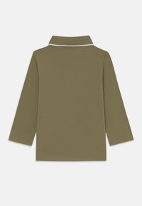 Olivgrön långärmad polo med en texturerad tyg, som har en vit kantad krage och ingen synlig logotyp.