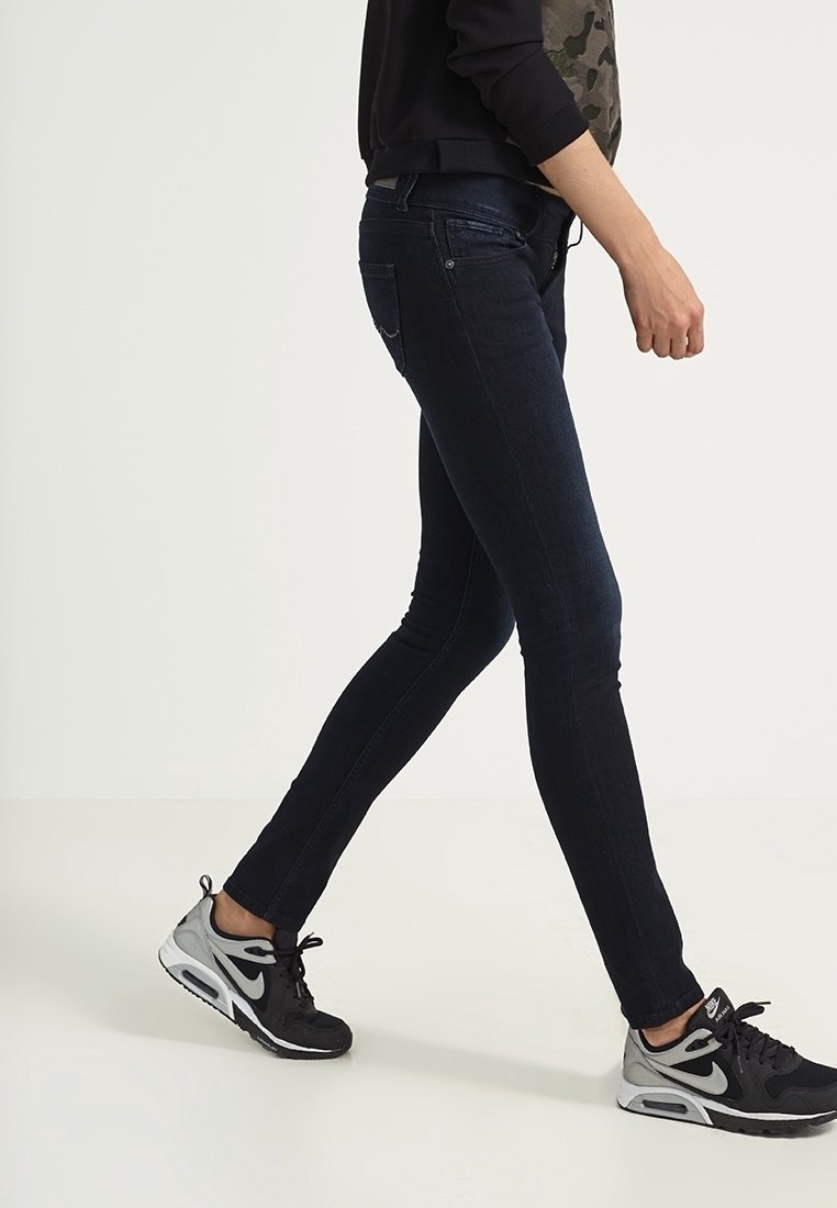 Tunna mörkblå jeans med en slät textur och subtila sömnadsdetaljer, tillsammans med svarta sportskor.