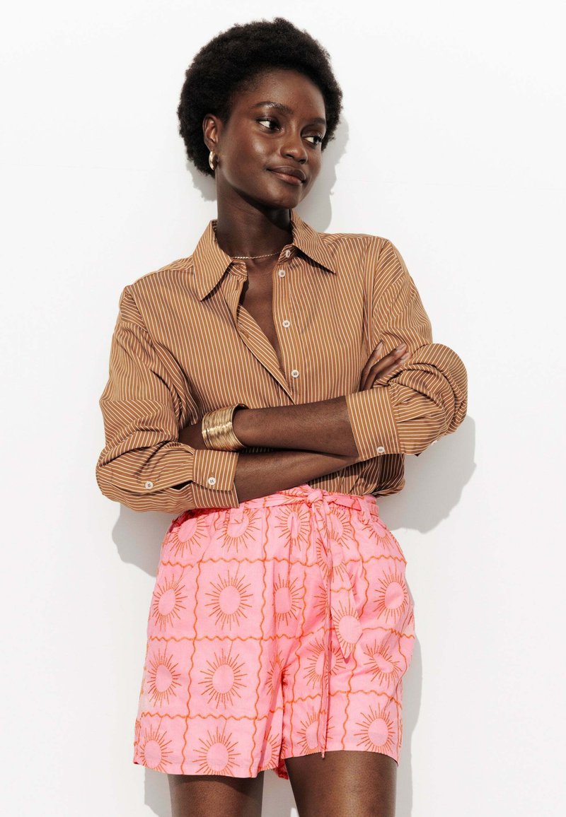 Chemise rayée marron avec détails de boutons, associée à un short rose avec un motif de soleil et une taille élastique. Texture de tissu lisse.