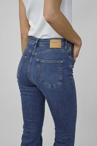 Sininen farkkutakki on slim fit -mallista, keskikorkea vyötärö, takataskut ja nahkatarra, jossa lukee "OMA PERUSTYYPPI".