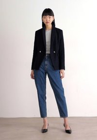 Zwarte dubbelzijdige blazer met zilveren knopen, grijs T-shirt eronder, hoge taille blauwe denim jeans, zwarte pointed-toe hakken.