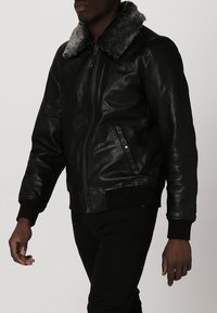 Schwarze Lederbomberjacke mit grauem Fellkragen, gerippten Bündchen und einem Bund, ausgestattet mit einem Reißverschluss vorne und einer Brusttasche.