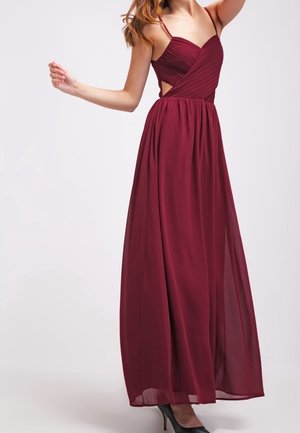 Bordeauxrode maxi-jurk met een nauwsluitend lijfje, kruisvormige bandjes en een vloeiende, doorschijnende rok. Voorzien van uitsnijdingen aan de zijkanten en een zachte textuur.