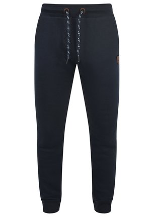 Navy jogger pants made from soft material. Features a drawstring waist with metal eyelets and ribbed cuffs. Includes a small logo patch.