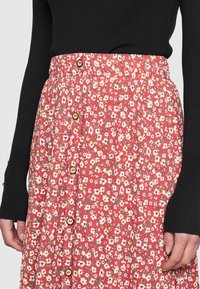 Floral midi skirt with a pink background, white and yellow flowers, elastic waist, and brown buttons down the front. Soft fabric texture.