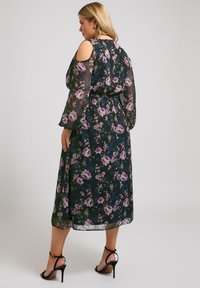 Blommig, svart maxiklänning med kallaxlar och genomskinliga långärmar, livfulla lila och gröna mönster, åtdragen midja och ankelsandaler.