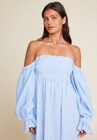 Lys blå av-skulder kjole med puffede ermer, med en smokkebodice og et rutete mønster. Myk lettvektig stoff.