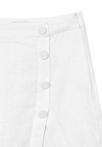Jupe en lin blanche avec un fermoir à boutons sur le devant et une fermeture à glissière latérale dissimulée, ornée de grands boutons recouverts de tissu.