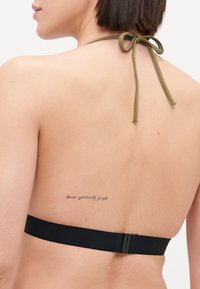 Haut de bikini noir à halter avec un lien de fermeture vert et une sangle ajustable. Présente un tatouage dans le dos et une texture lisse.