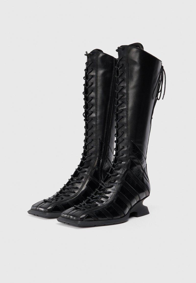 Schwarze Lederstiefel bis zum Knie mit schnürbarem Vorderteil, strukturierten Einsätzen und kleinem Stacked-Heel. Glatte Oberfläche mit kontrastierenden Akzenten.
