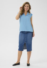 Svetlomodrá blúzka s riaseným výstrihom, kombinovaná s denimovou ceruzkovou sukňou so predným rozparkom. Čierne ploché topánky dotvárajú outfit.