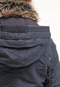 Marinblå tygjacka med furfoder i huvan, ribbat krage och texturerad kroppsdetaillering. Sticksömmar på baksidan.