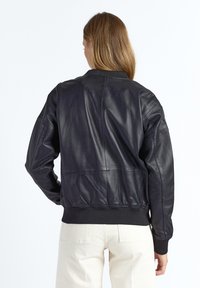 Sort læderbomberjakke med ribbet talje og manchetter, der har en glat tekstur og en oversize silhuet. Set bagfra.