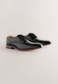 Black leather dress shoes with closed lacing, subtle perforated detail on the sides, pointed toe, and wooden sole.