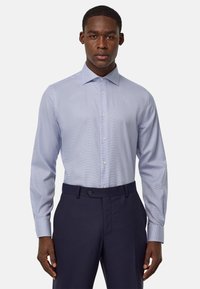 Camicia a quadri blu chiaro con maniche lunghe e colletto a punta, abbinata a pantaloni blu scuro. Tessuto liscio e design aderente.