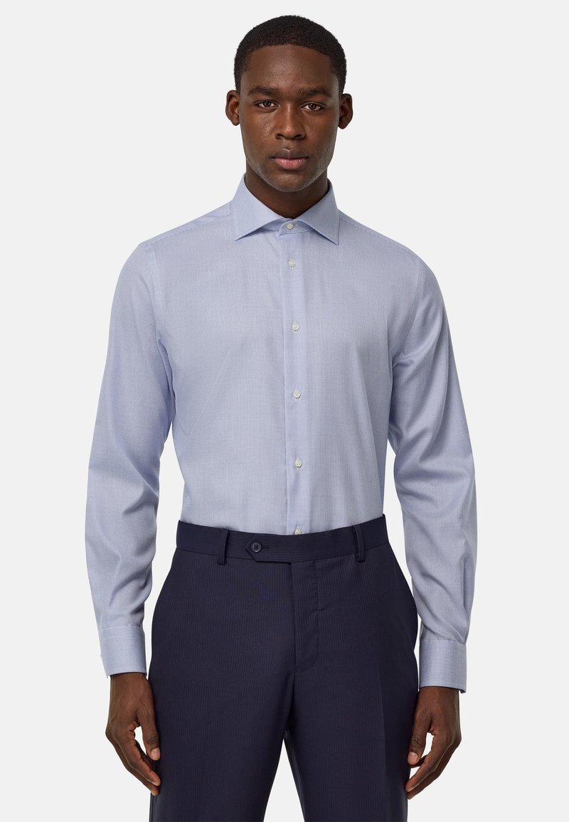 Camicia a quadri blu chiaro con maniche lunghe e colletto a punta, abbinata a pantaloni blu scuro. Tessuto liscio e design aderente.