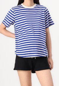 Camiseta de algodón con rayas horizontales blancas y azules, cuello redondo, mangas cortas y un ajuste relajado, combinada con pantalones cortos negros.
