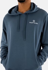 Sudadera con capucha de color azul marino hecha de una tela suave, que cuenta con un bolsillo canguro, capucha con cordón y un logo bordado en blanco en el pecho.