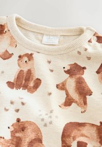 Pull léger beige avec un tissu texturé, mettant en avant des illustrations de ours en aquarelle ludiques dans des tons de brun et de pêche. Design à col rond avec des pressions.