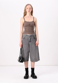 Brun tanktopp med tynne stropper, kombinert med løse grå denim culotted. Modellen holder en liten svart håndveske og har på seg svarte snørebåndsstøvler.