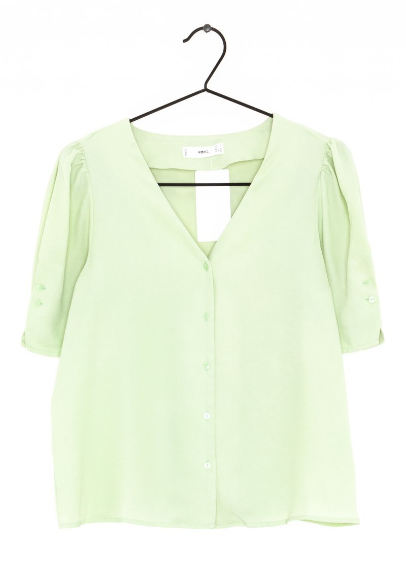 Blouse vert clair à manches courtes bouffantes, encolure en V et fermeture à boutons sur le devant. Tissu lisse avec un léger éclat, suspendue à un crochet noir.