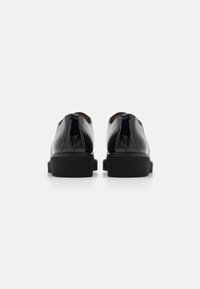 Scarpe in vernice nera con una finitura liscia, tacco basso a blocco, retro arrotondato e dettagli minimi.