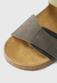 Γκρι δερμάτινο σανδάλι με δύο φαρδιές λωρίδες, μία υφή και μία λεία. Διαθέτει φιάπα από φελλό και μαλακό καφέ πάτο.