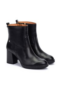 Botas de tobillo de cuero negro con un tacón robusto, que cuentan con costuras laterales y lengüetas en la parte trasera para facilitar su puesta. Textura suave en toda la superficie.