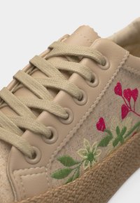 Baskets beige avec semelle tissée, ornées de feuilles vertes brodées et de fleurs rouges, avec des lacets beiges passés dans six œillets.