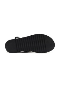 Semelle extérieure en caoutchouc noir avec un motif strié, dotée d'un bout fermé et d'une sangle réglable, soutenue par un talon plat.