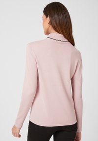 Helles rosa Langarmshirt mit umgeschlagenem Kragen und schwarzem gewelltem Saum. Glatte Textur, taillierte Passform und verlängertes Rückenteil.