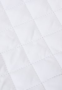 Tejido blanco acolchado con un patrón de cuadrícula y costuras visibles. La textura es suave y ligeramente reflectante.