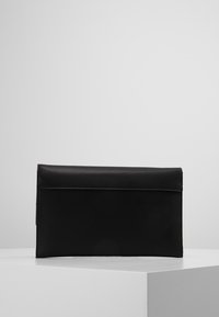 Svart rektangulär läderklutchväska med flikstängning, placerad på en vit yta mot en enkel ljusgrå bakgrund.