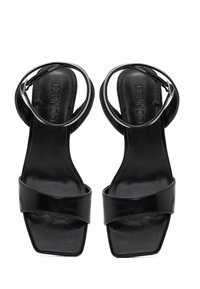 Mustat korkokengät, joissa on nelikulmainen varvasosa, leveä ristikkäin nauha ja nilkkanyöri. Valmistettu sileästä nahasta kiiltävällä pinnalla.