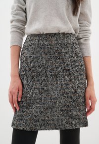 Jupe en laine en chevrons gris et noir avec des touches de marron. Design ajusté avec une texture subtile et une coupe au genou. Taille plate.