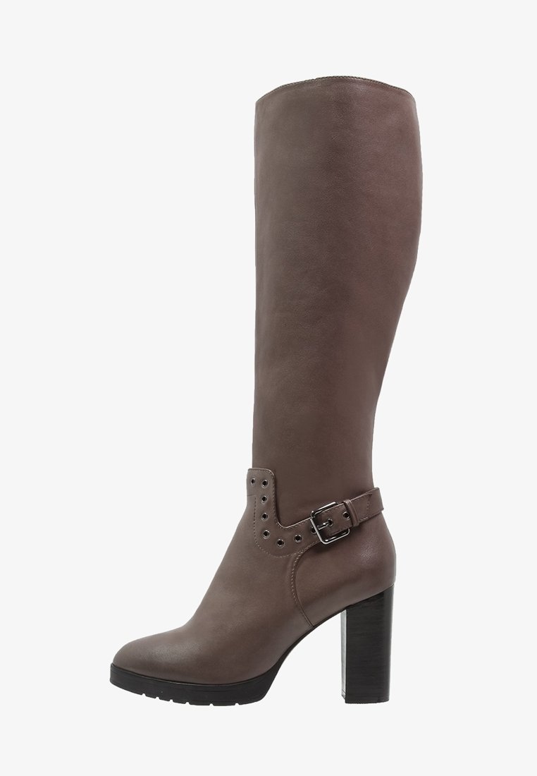 Botte en cuir marron montante avec une tige large, détail en boucle et accents en clous. Dotée d'un talon épais noir et d'une texture lisse.