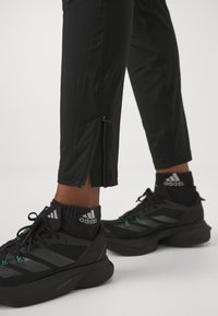 Czarne spodnie sportowe z zamkiem błyskawicznym przy kostkach, zestawione z czarnymi sneakersami z zielonymi akcentami i teksturowaną siateczkową cholewką.