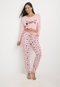 Conjunto de pijama rosa que incluye una parte superior de manga larga anudada con estampado gráfico y pantalones impresos con varios diseños coloridos, incluyendo pingüinos y cócteles.