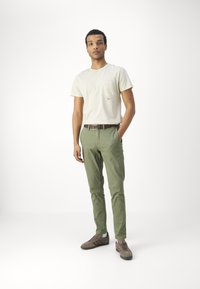 Camiseta de color beige claro con bolsillo, pantalones verdes de corte slim y zapatillas marrones. Diseño sencillo con detalles minimalistas y texturas suaves.