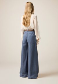 Hellblaue weit geschnittene Hosen aus weichem Stoff, ausgestattet mit zwei Gesäßtaschen und einer hohen Taille, kombiniert mit einer durchsichtigen weißen Bluse.