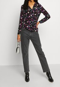 Blouse noire à fleurs avec des manches longues, ornée de fleurs violettes et bleues, associée à un jean droit gris et des bottines noires.