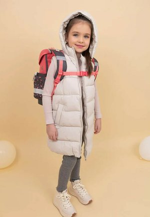 Puffige cremefarbene Weste mit Kapuze, kombiniert mit einem rosa und grau gemusterten Rucksack. Graue Leggings und weißes Sneakers mit beigen Akzenten.