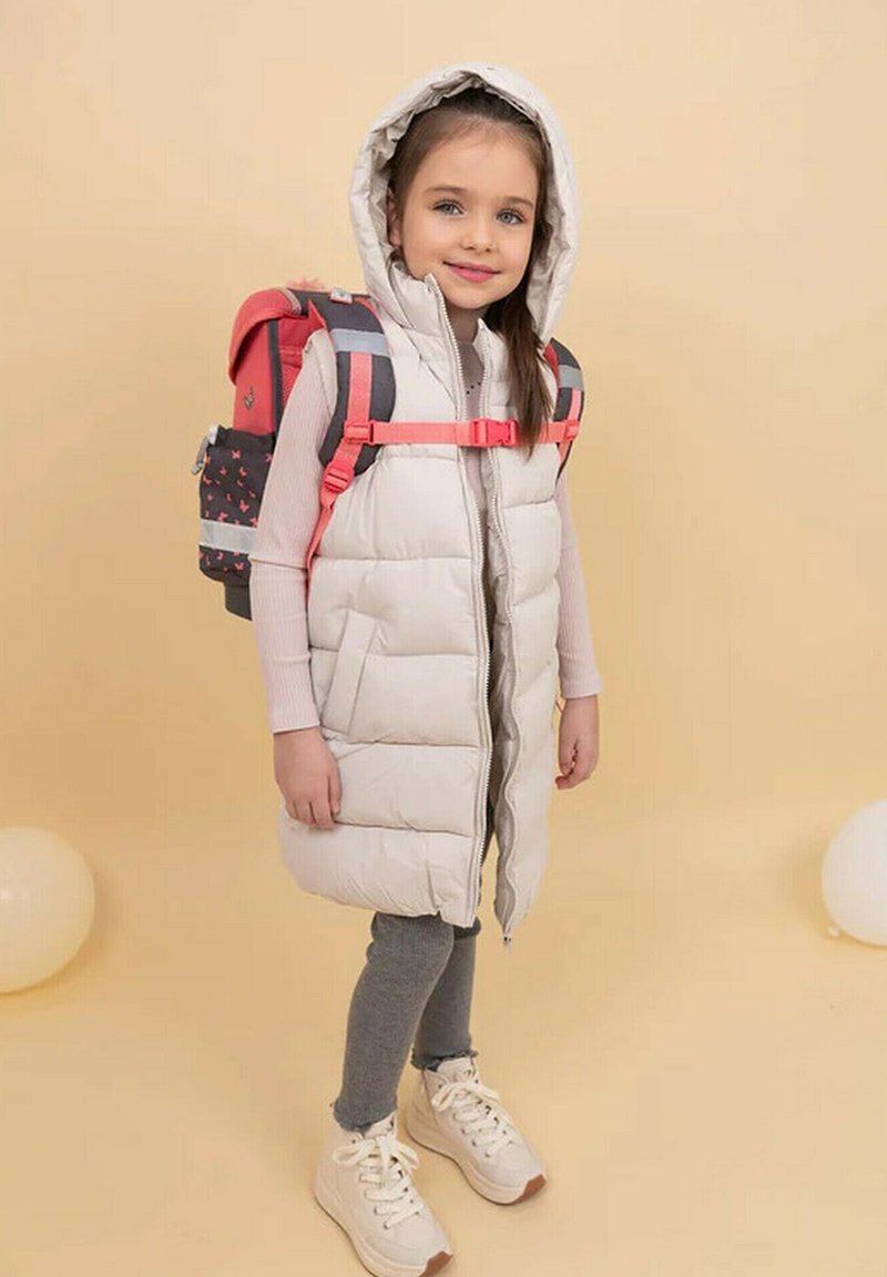 Puffy cream-colored vest with a hood, paired with a pink and gray patterned backpack. Gray leggings and white sneakers with tan accents.
