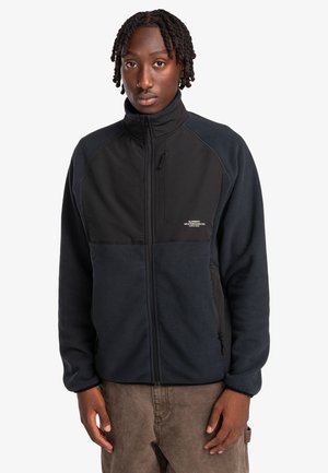 Fleece jacket with a zip front, featuring a dark navy body and black panels. Includes a small logo on the chest and zippered pockets.