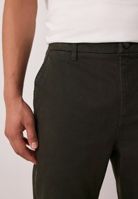 Dark green pants made of textured fabric, featuring a button closure, two side pockets, and a fitted design.