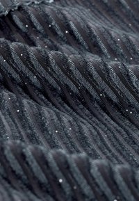 Textilní látka v černé barvě s vyvýšenými vertikálními pruhy a jemným třpytem. Měkká textura s kombinací huňatých a hladkých materiálů.