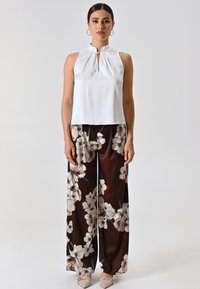 Top en satin blanc avec un détail en trou de serrure, associé à un pantalon large à imprimé floral marron. Texture lisse et motif floral élégant.