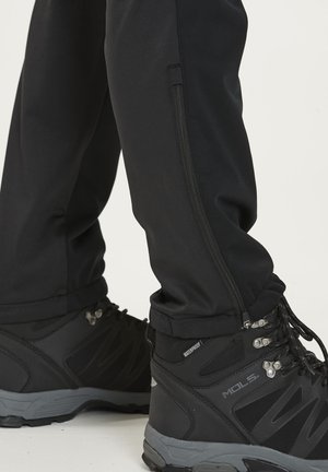 Musta pehmeäpintainen housut, joissa on sivuvetoketjulliset taskut, yhdistettynä mustiin vedenkestäviin vaelluskengiin, joissa on harmaita yksityiskohtia ja teksturoitu pohja.