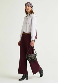 Camicia bianca a maniche lunghe, pantaloni larghi color melanzana, borsa nera decorata, stivali neri con tacco, sciarpa fantasia, accessori dorati.